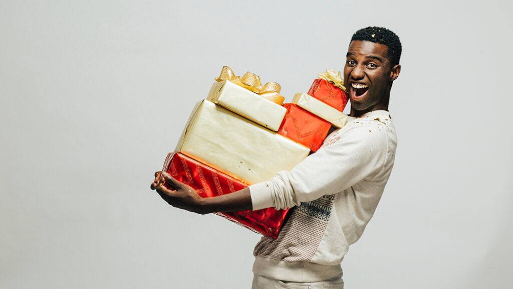 Porträtt av en upphetsad ung man som bär många gåvor, isolerad på vit studiobakgrund