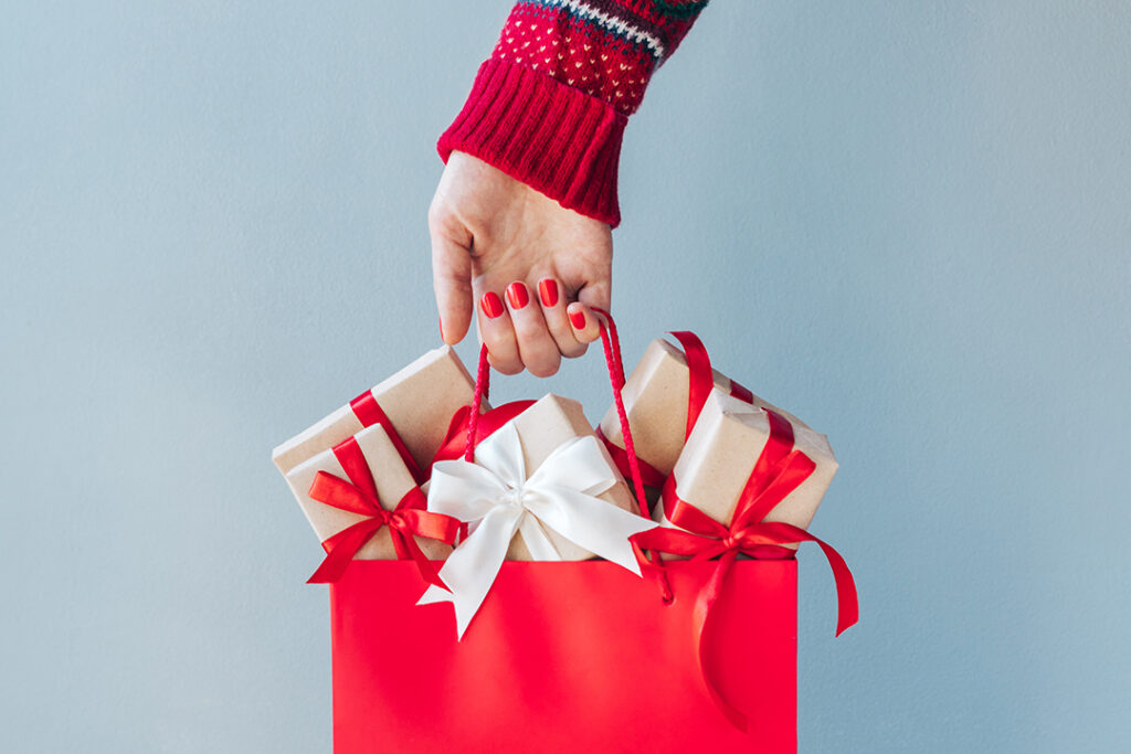 Beskuren bild av kvinnlig hand med röda polerade naglar som håller shoppingväskan full av julklappsförpackningar