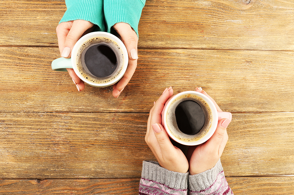 Kvinnliga händer som håller koppar kaffe på rustik träbordsbakgrund