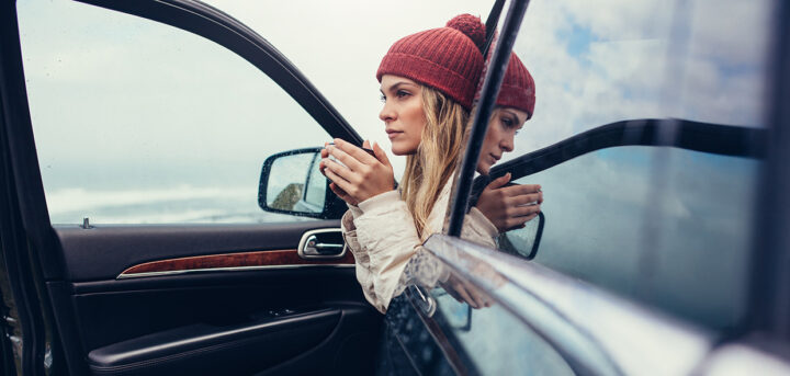 kvinna sitter i en bil dricker ur en mugg, vinter