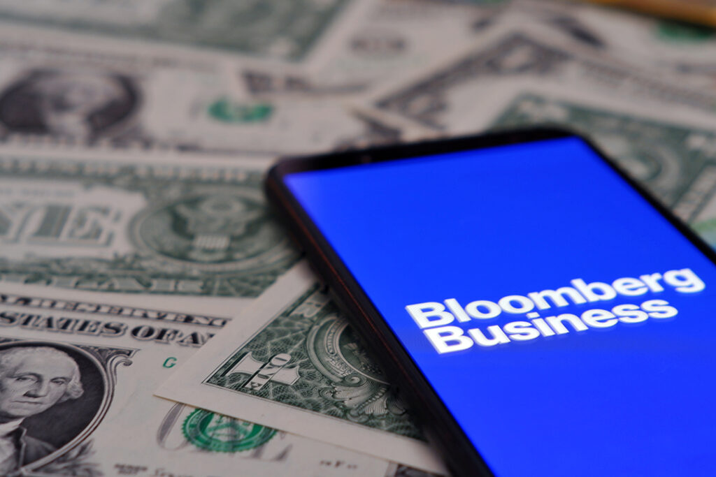 Mobiltelefon med Bloomberg-logotypen i skärmen, mobilen ligger på en massa pengar