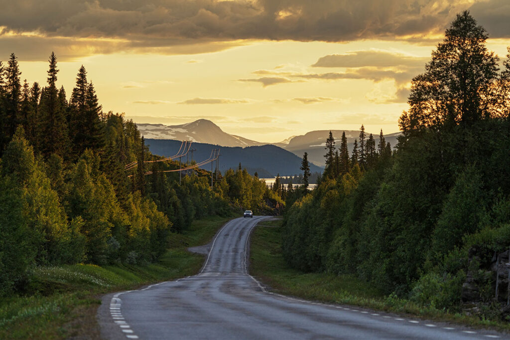 kvällsbild på en lång väg norra Sverige med fjäll i bakgrund