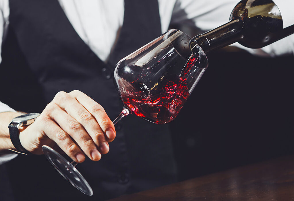 Närbild av sommelier som häller rött vin från flaska i glas