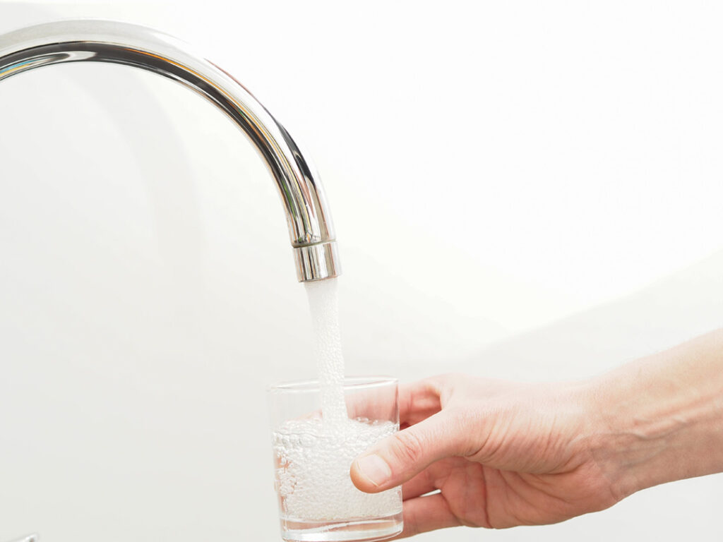 Hand med ett glas och hällande vatten i ett kök