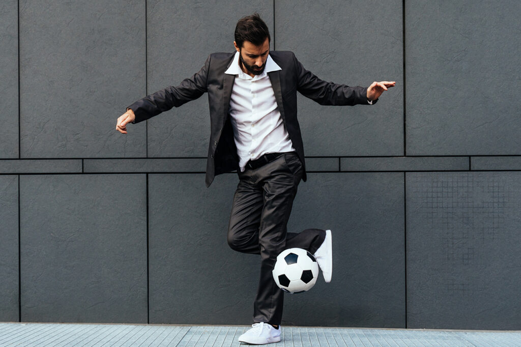 Bild av en affärsman och fotbollsspelare som gör trick med bollen på gatan. 