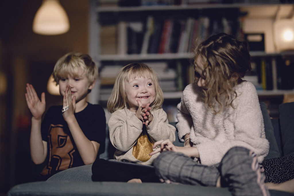 Glad handikappad flicka klappar medan hon sitter med sina syskon hemma