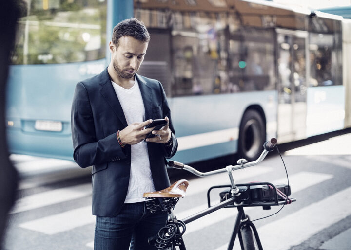 Affärsman som använder mobiltelefon medan han står med cykel på stadsgatan